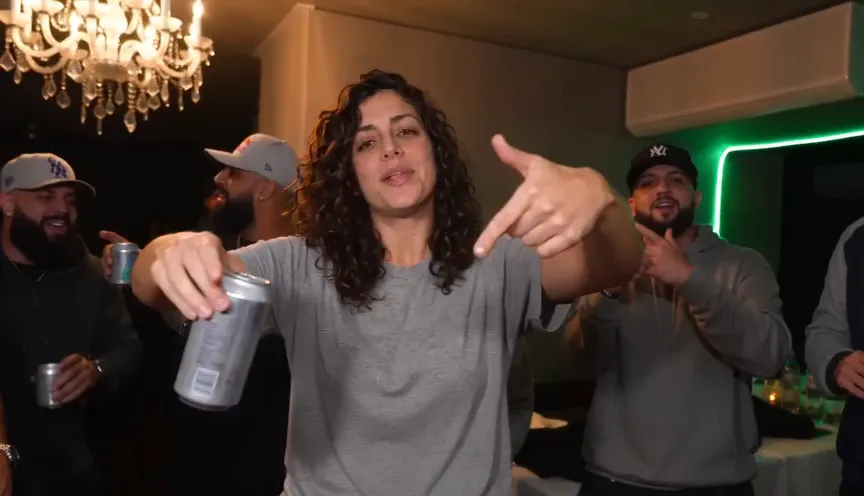 Burning Bridges AI video frame: a woman in a grey tee gives finger guns to the camera, can in hand, under a chandelier