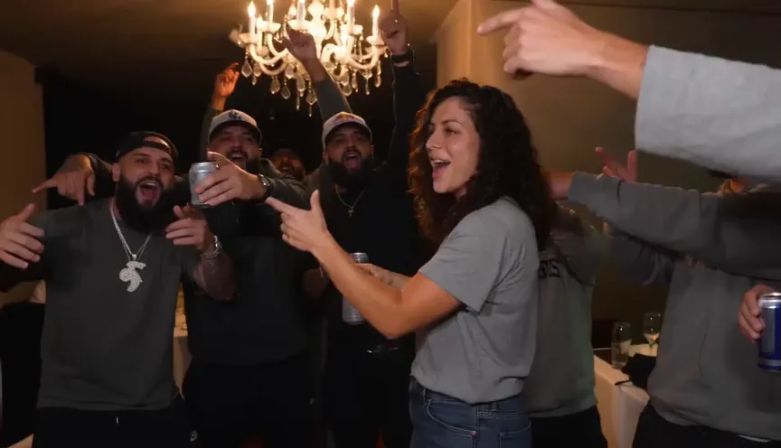 Burning Bridges AI video frame: the friends crowd in around her, cheering with drinks raised