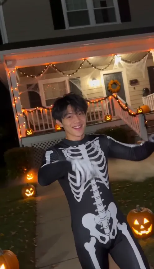 A young man in a black jumpsuit printed with white rib bones smiles on a Halloween street