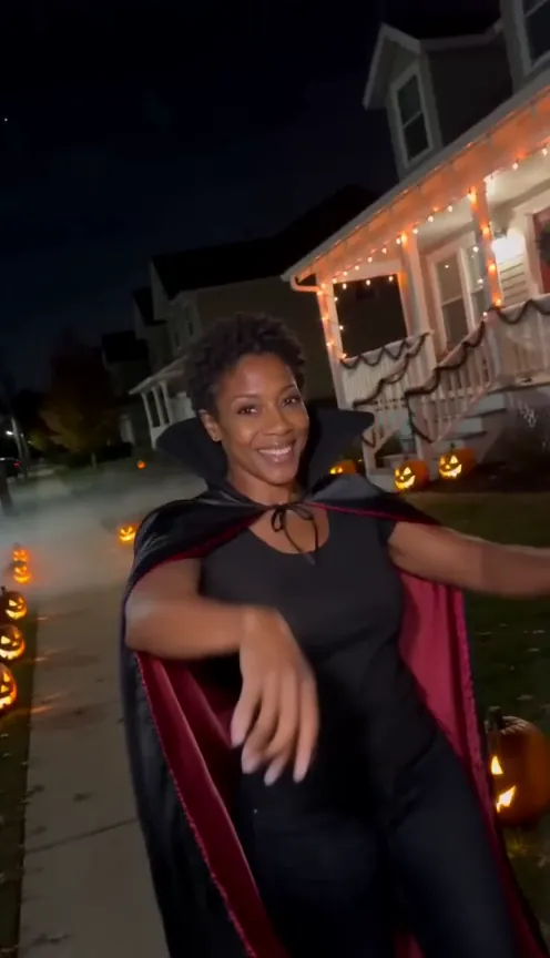 A woman in a black cape with a tall stiff collar and a red lining smiles at the camera at night
